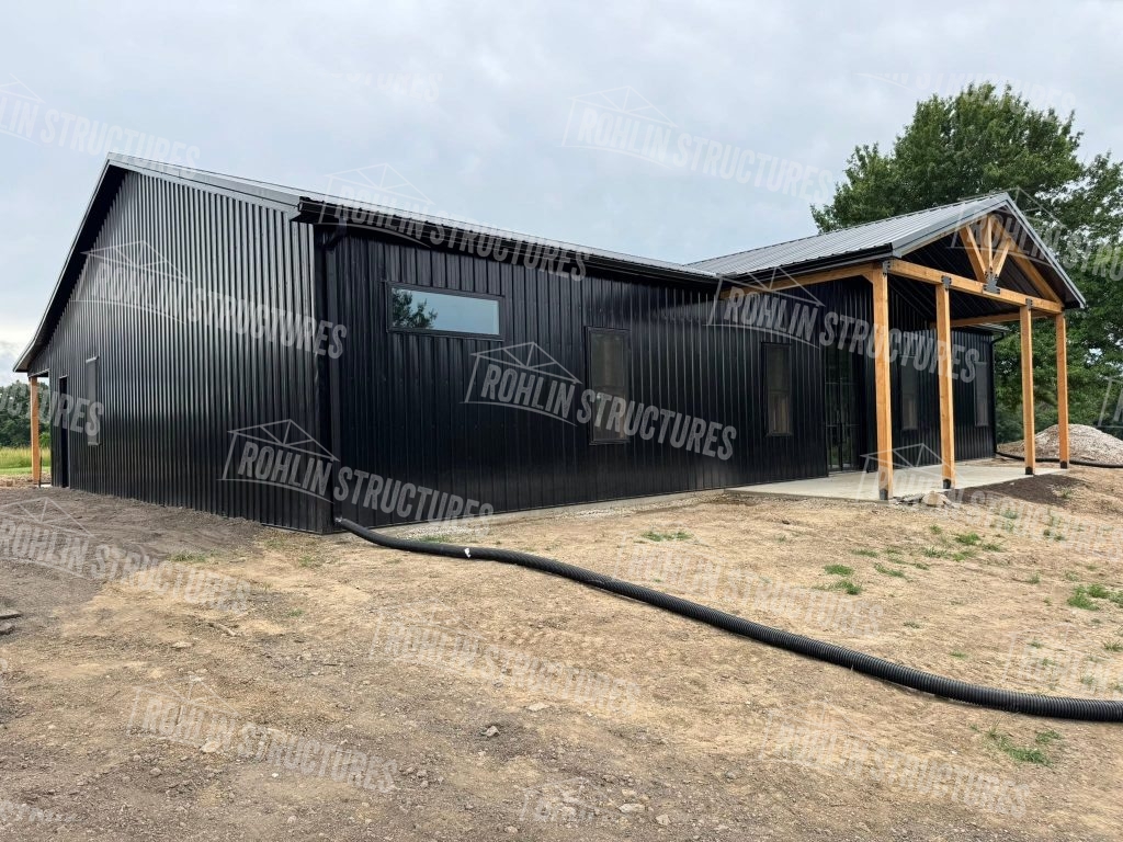 Rohlin Structures barndominium construction with black siding, timber framing, and a porch.