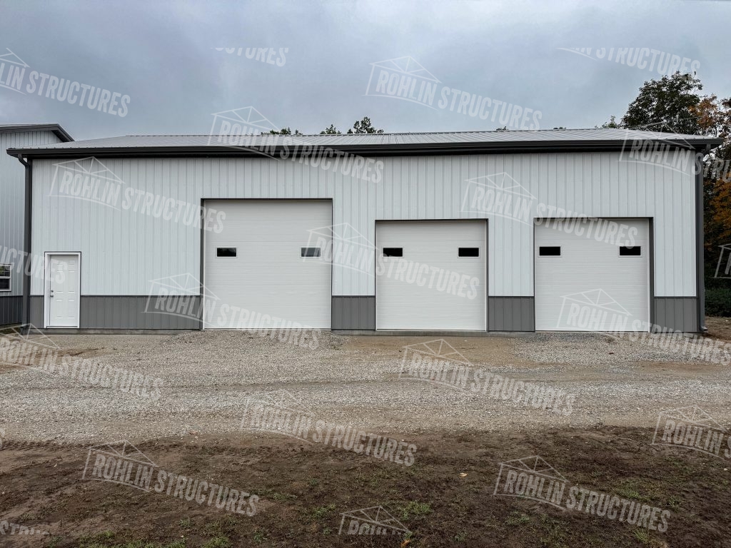 Custom white and gray pole barn garage with multiple overhead doors built by Rohlin Structures.