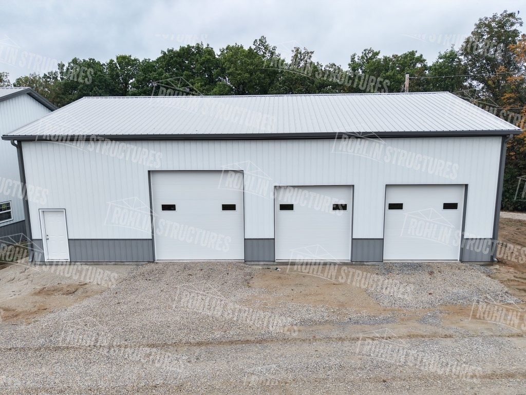 Custom pole barn workshop with white siding and three garage doors built by Rohlin Structures.